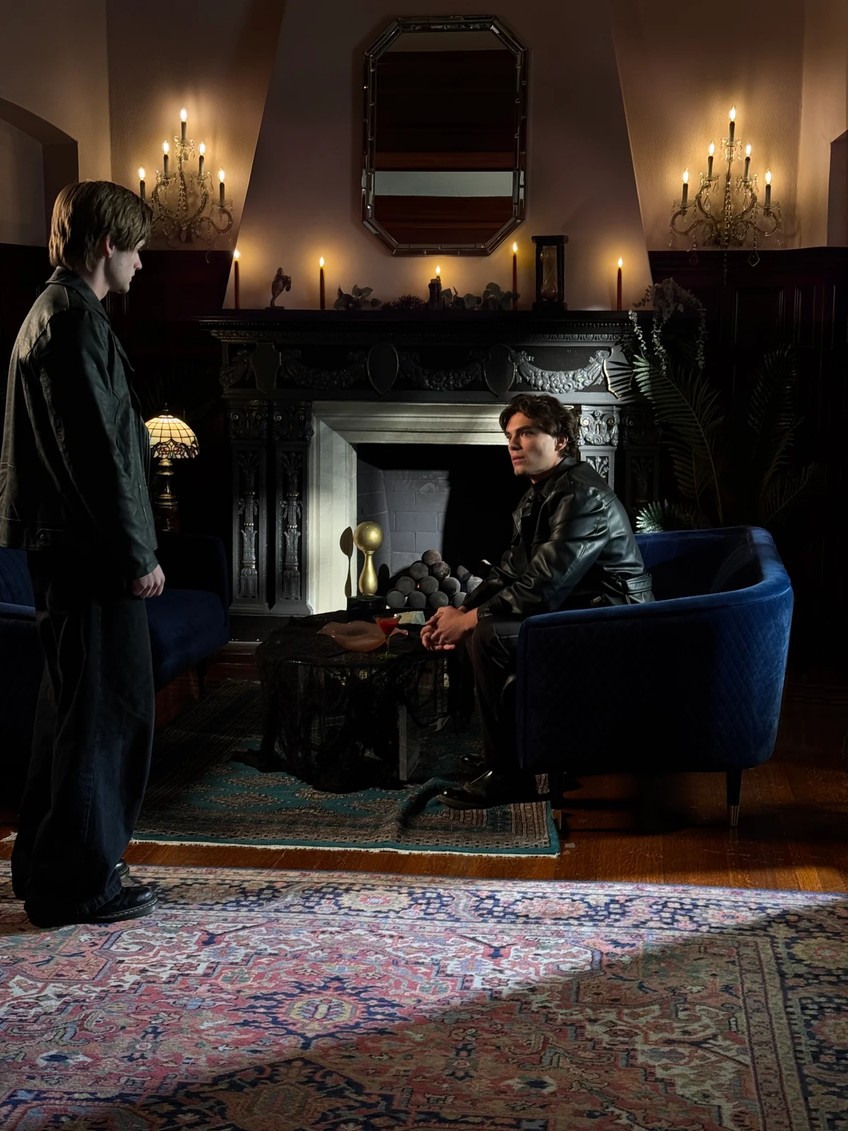 Two performers in a candlelit room with a black fireplace, blue seating and patterned rugs.